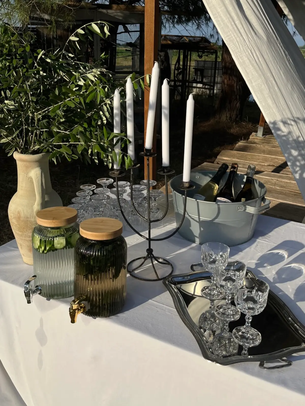 Table dressée en extérieur, carafes, verres et bougies au coucher du soleil